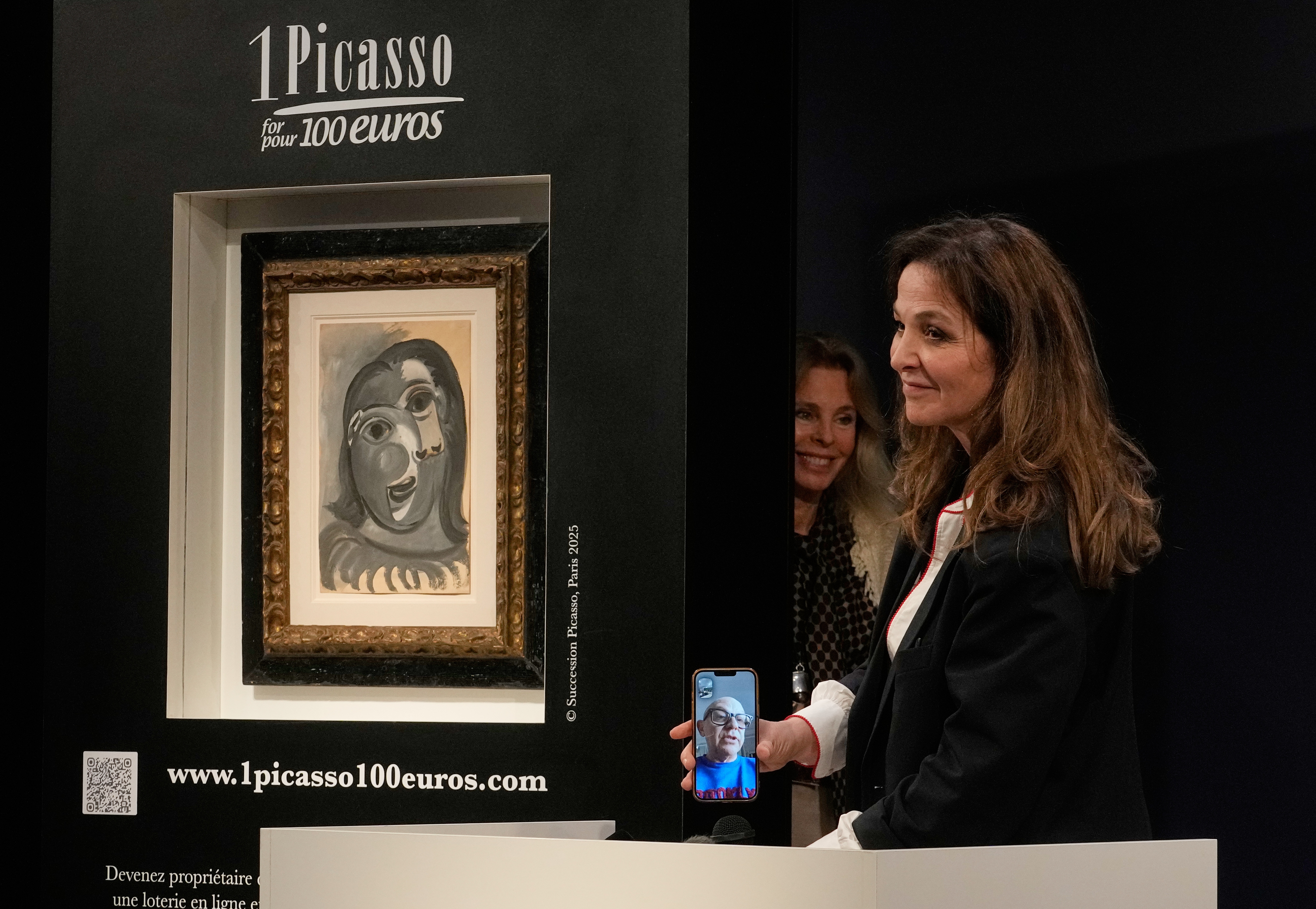 Peri Cochin, right, founder of "1 Picasso for 100 euros," speaks on the phone with the winner, Ari Hodara of Paris, next to the painting 